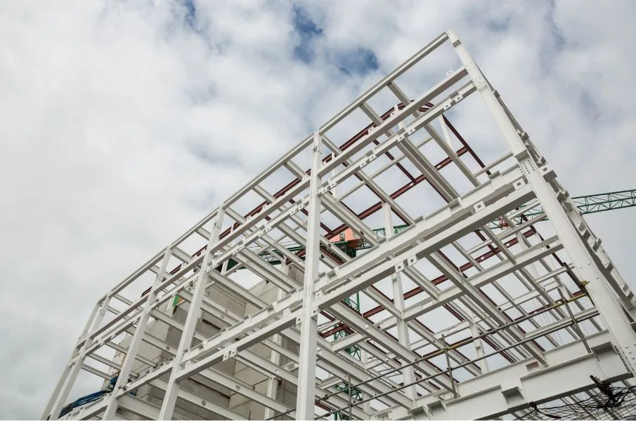 Structural steel frame with beams, columns, joists, and metal decking under construction.