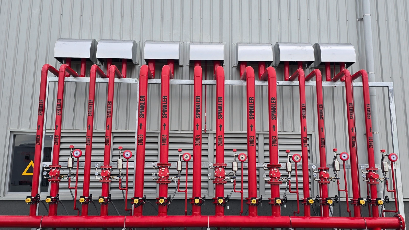 Industrial fire sprinkler piping, valves, and control assemblies installed on a building exterior.