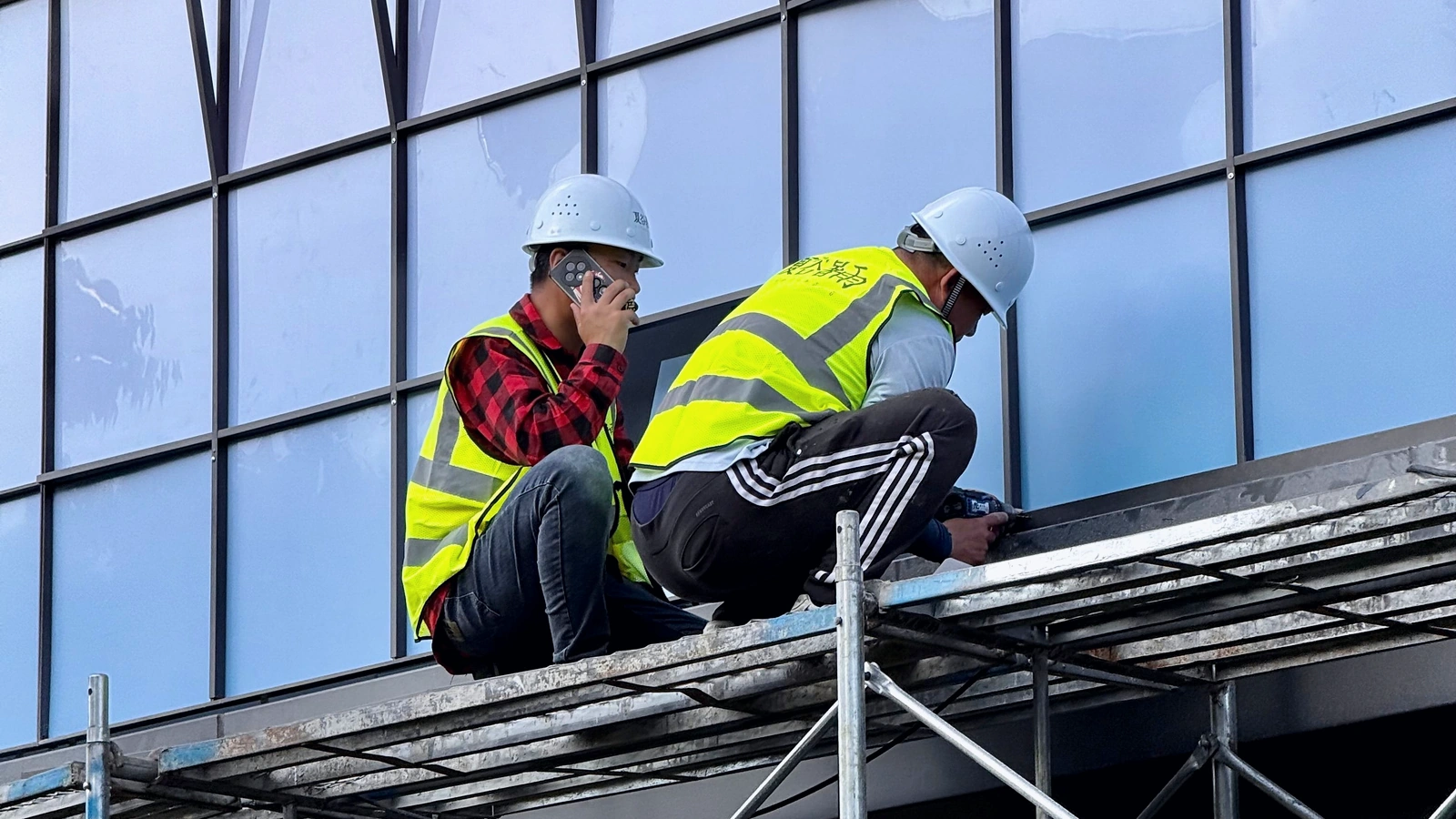 Glazing crew installing exterior window units from construction scaffolding.
