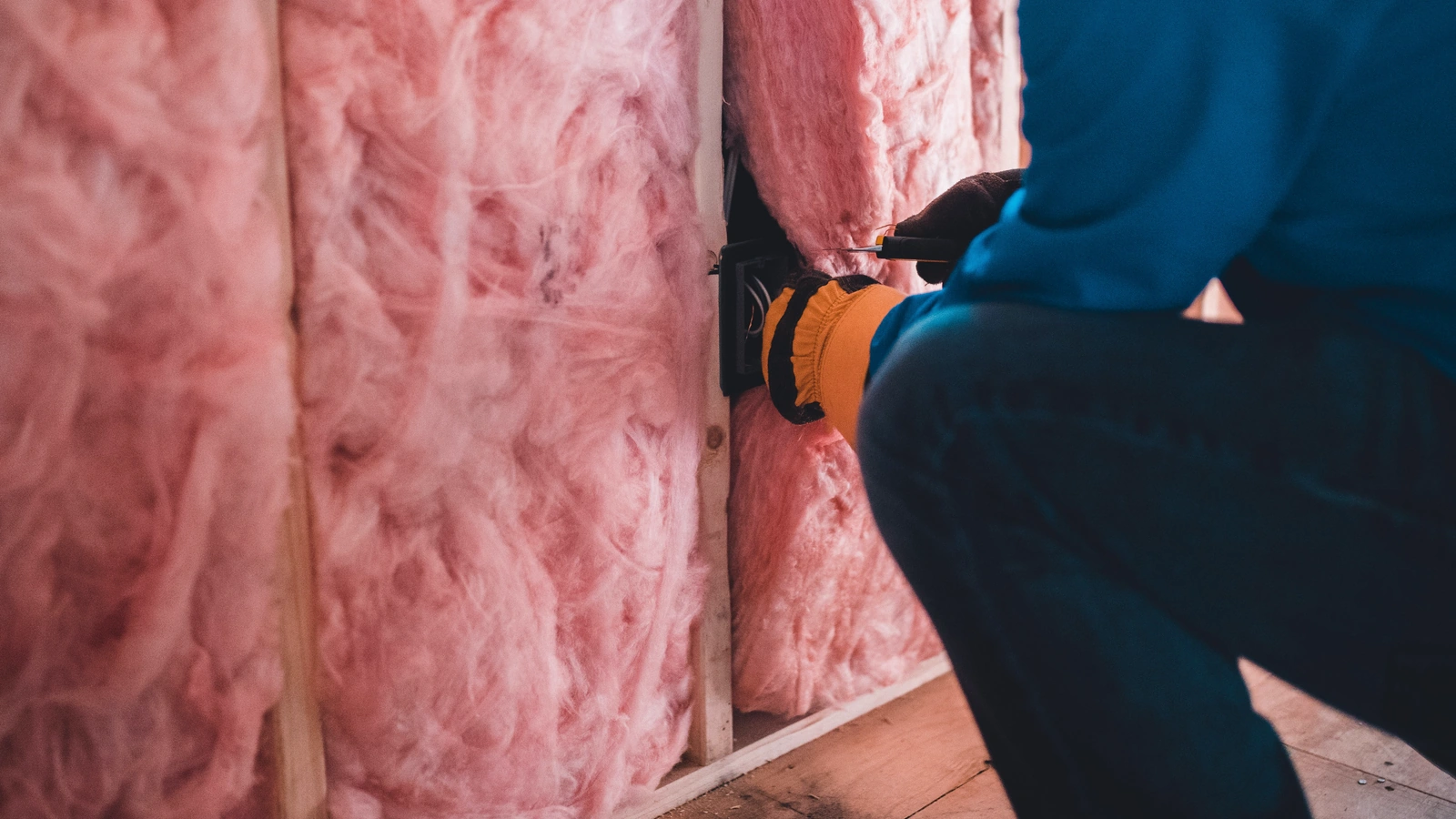 Construction worker installing fiberglass wall insulation between wood framing members.