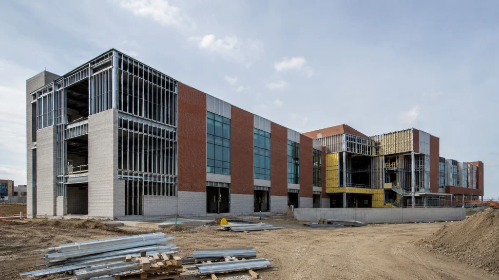 School or university building under construction with masonry, window systems, metal framing, and unfinished campus facilities.