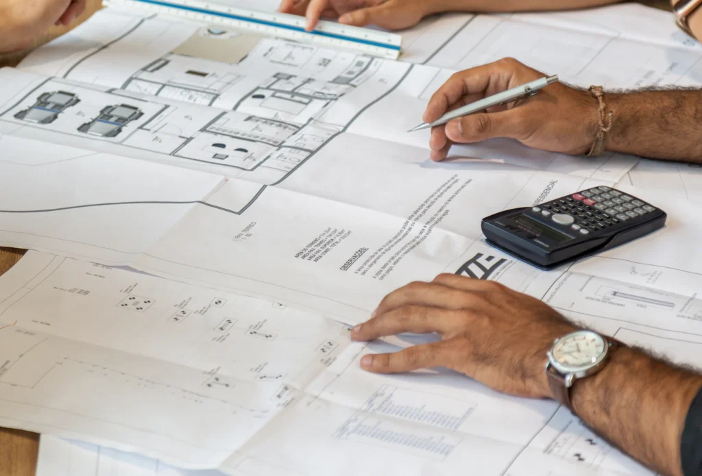 Construction professionals reviewing architectural and engineering drawings with a calculator during preconstruction planning